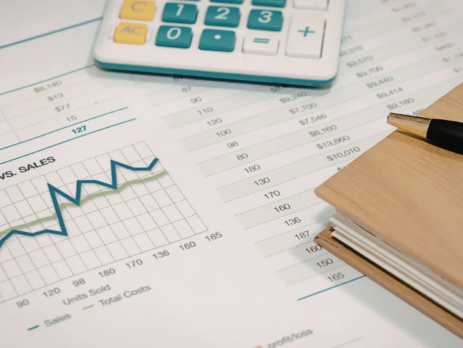 Vista en primer plano de herramientas de análisis de datos y retorno de inversión sobre un escritorio de madera con una oficina moderna difuminada de fondo.